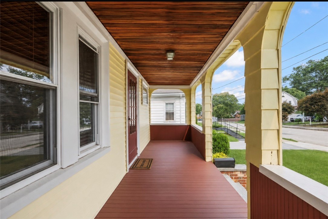 Covered front porch with reddish decking, a dark wood ceiling, and arched supports.