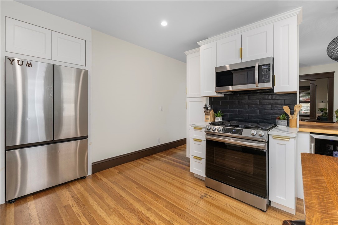 Kitchen with white cabinets, stainless steel appliances, black tile backsplash, and hardwood floors.