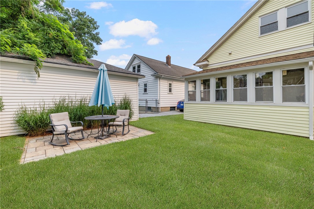 Backyard with a stone patio, outdoor seating, blue umbrella, and lawn.