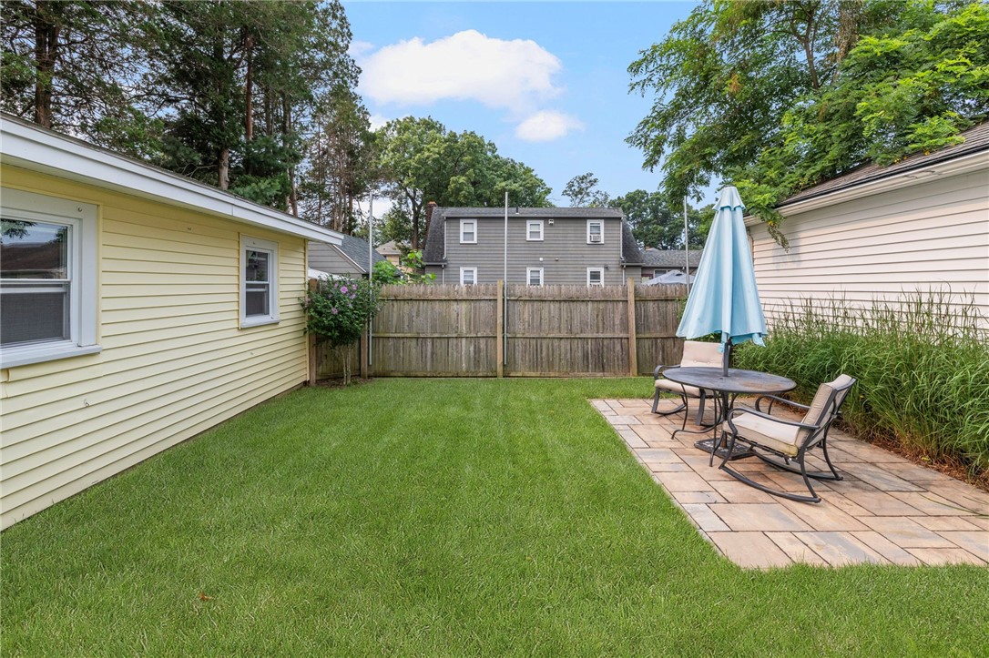 Fenced backyard with a broad lawn and stone patio seating beneath a blue umbrella.