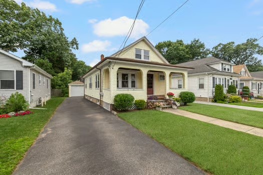 Yellow one-story house with a covered front porch, steep gabled roof, and long driveway to a detached garage.