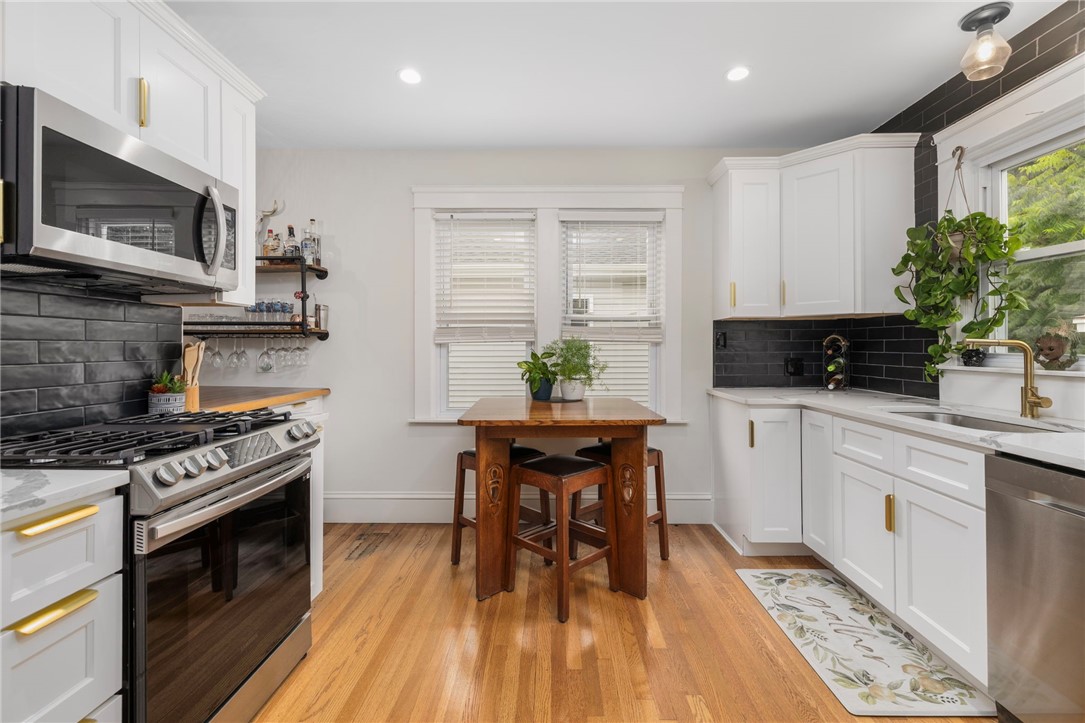 Kitchen with white cabinets, black tile backsplash, stainless steel range, and a wooden table by two windows.