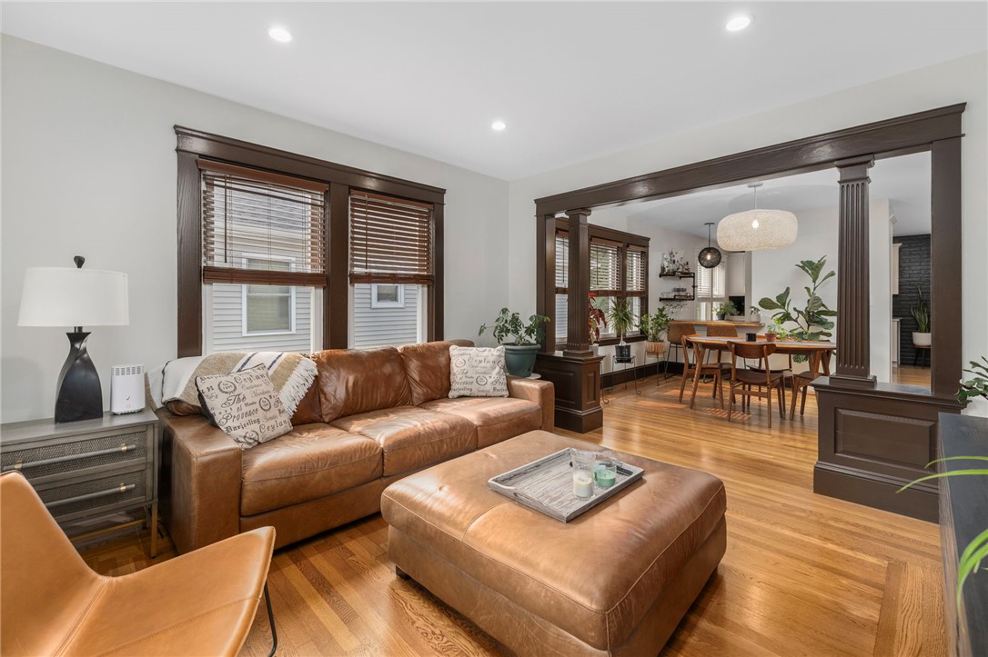 Living room with brown leather seating, hardwood floors, and dark wood trim opening to a dining area.