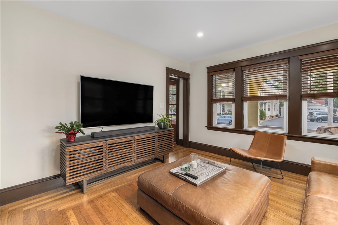 Living room with a large TV, brown leather seating, hardwood floors, and wide windows.