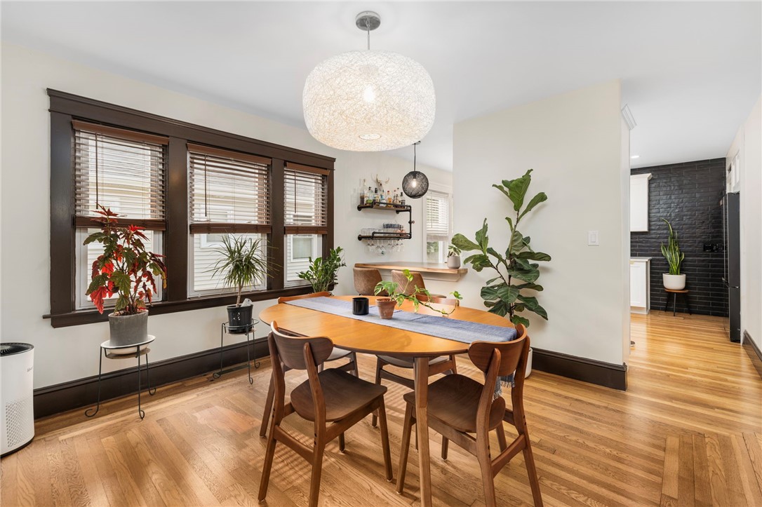 Dining room with a round wooden table, hardwood floors, dark-trimmed windows, and a woven pendant light.
