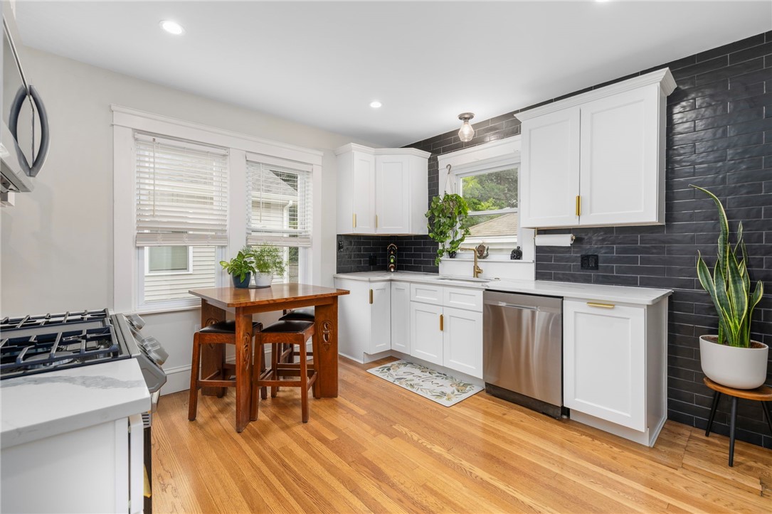 Kitchen with white cabinets, black tile backsplash, stainless dishwasher, and a small wooden dining table.