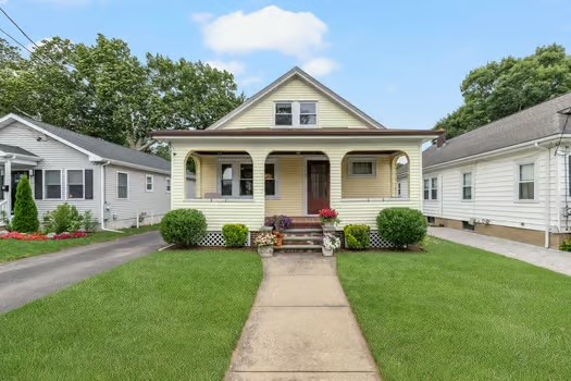 Yellow house with a covered porch, front walkway, and green lawn.