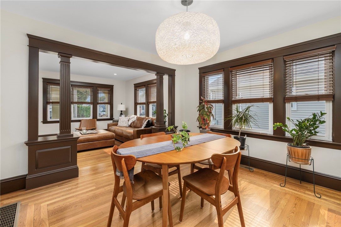 Dining room with a round wooden table, hardwood floors, and a columned opening to the living room.