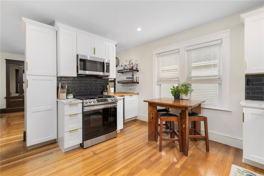 Kitchen with white cabinets, stainless steel appliances, dark tile backsplash, hardwood floors, and a wooden dining table.