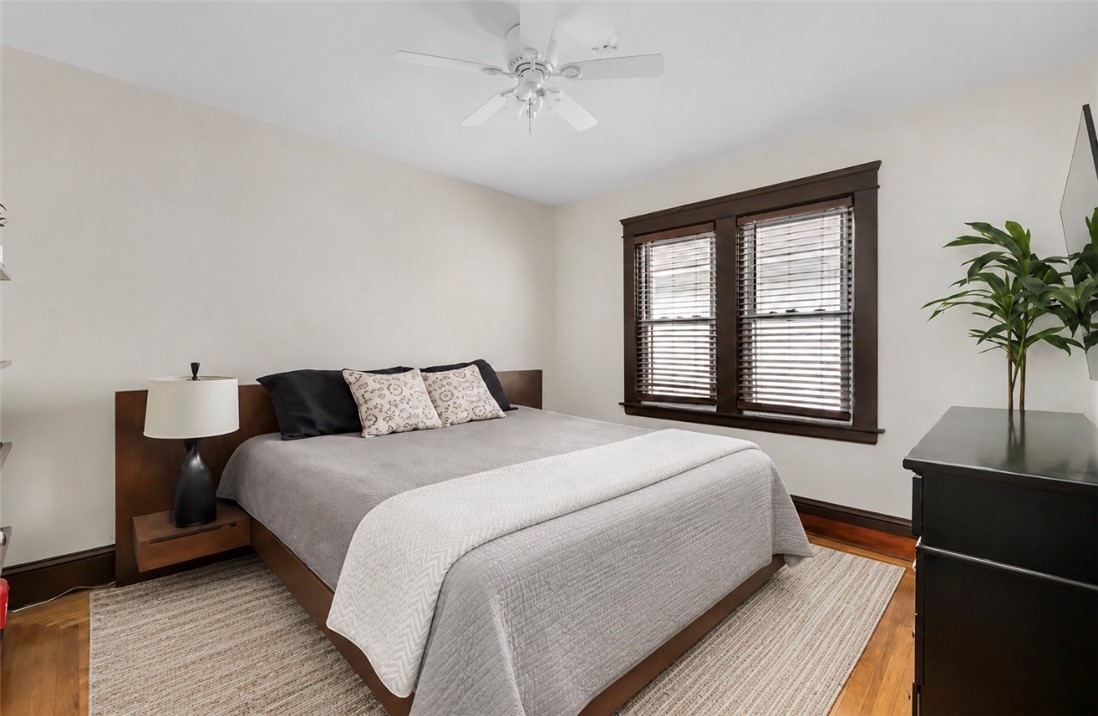 Bedroom with a gray-and-white bed, dark wood trim, and hardwood floors.