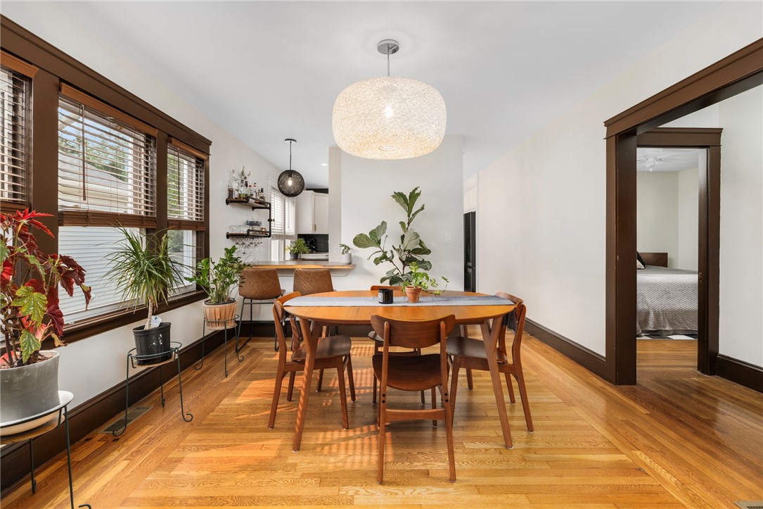 Dining room with a wooden table, hardwood floors, large windows, and plants.