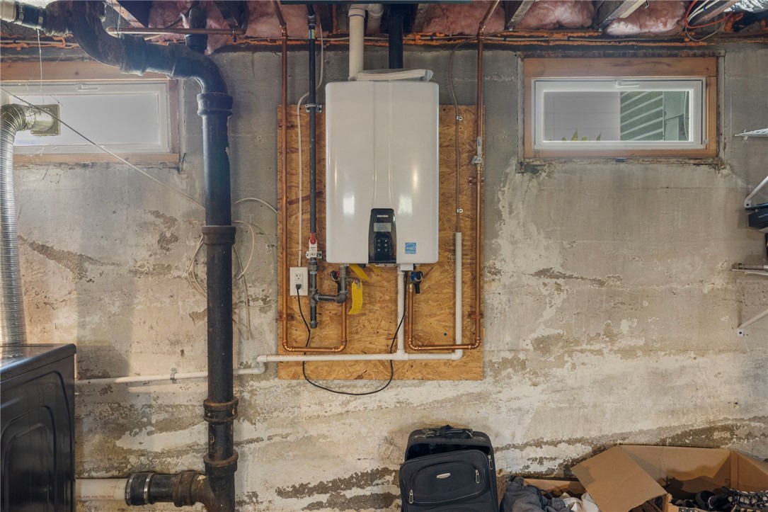 Basement utility area with a wall-mounted tankless water heater, exposed pipes, and rough concrete walls.