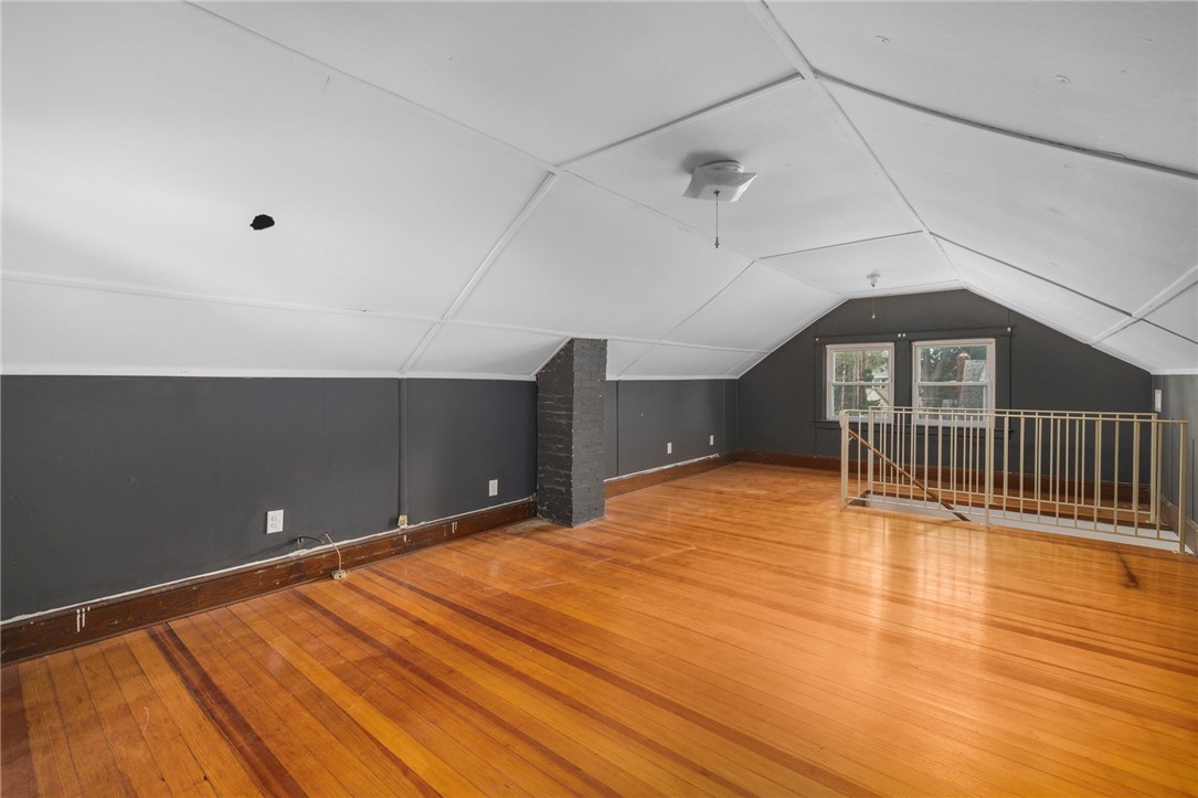 Finished attic loft with polished hardwood floors, sloped ceiling, brick column, and railing around the stair opening.