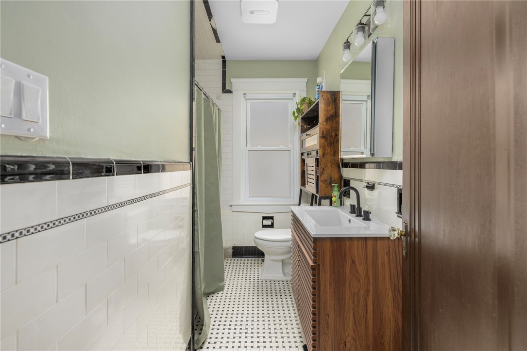 Bathroom with a wood vanity, white tile, and black-and-white mosaic floor.
