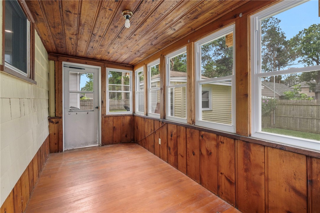 Enclosed porch with wood-paneled walls and ceiling, plank flooring, and windows overlooking a fenced yard.