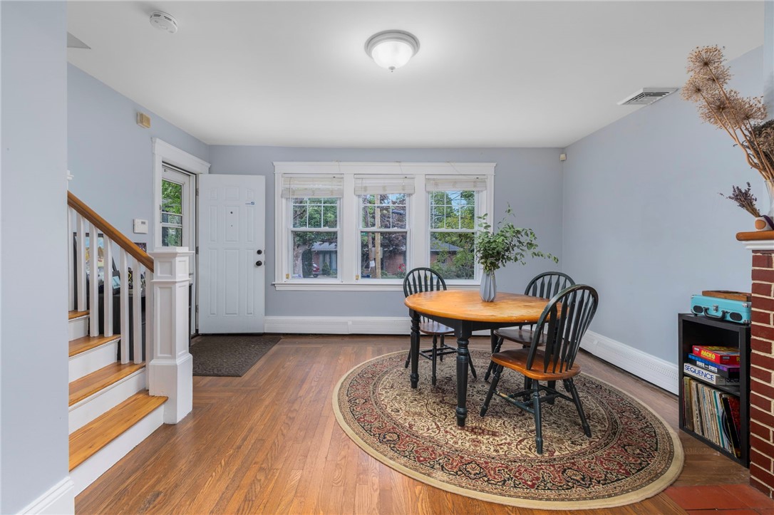 Dining room with a round wooden table, patterned rug, hardwood floors, and three windows.
