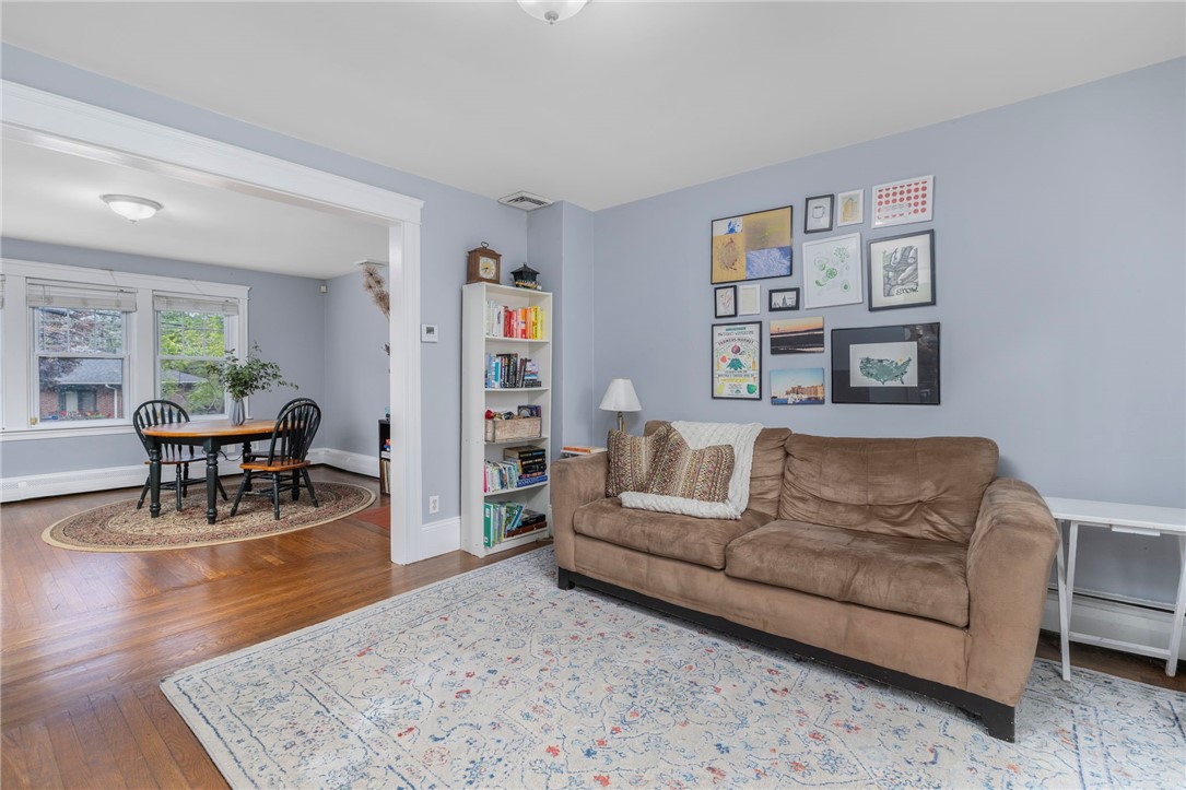 Living room with a brown sofa and gallery wall, opening to a dining area with large windows.