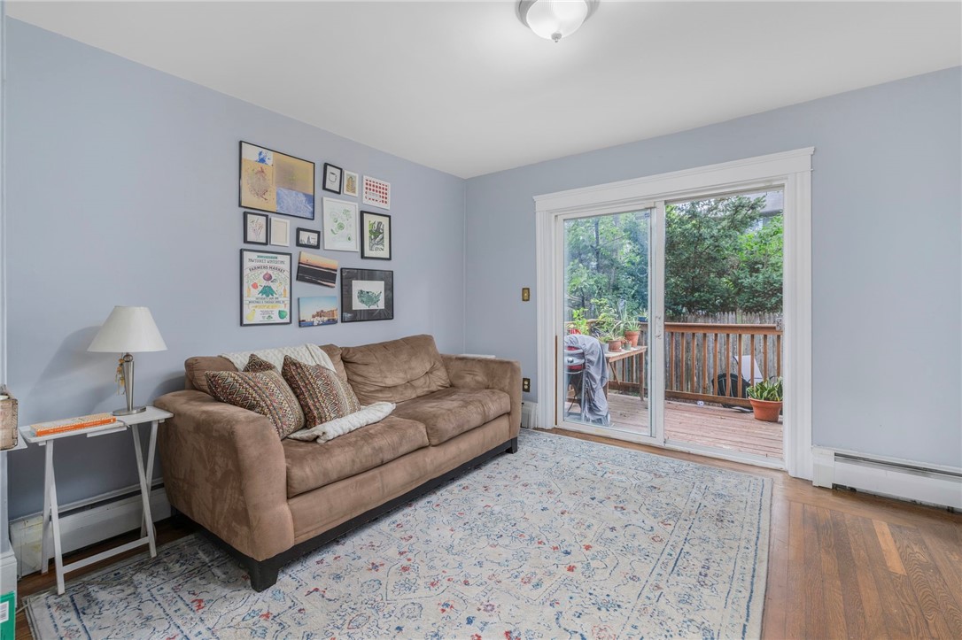 Living room with a brown sofa and patterned rug beside a glass door opening onto a leafy deck.