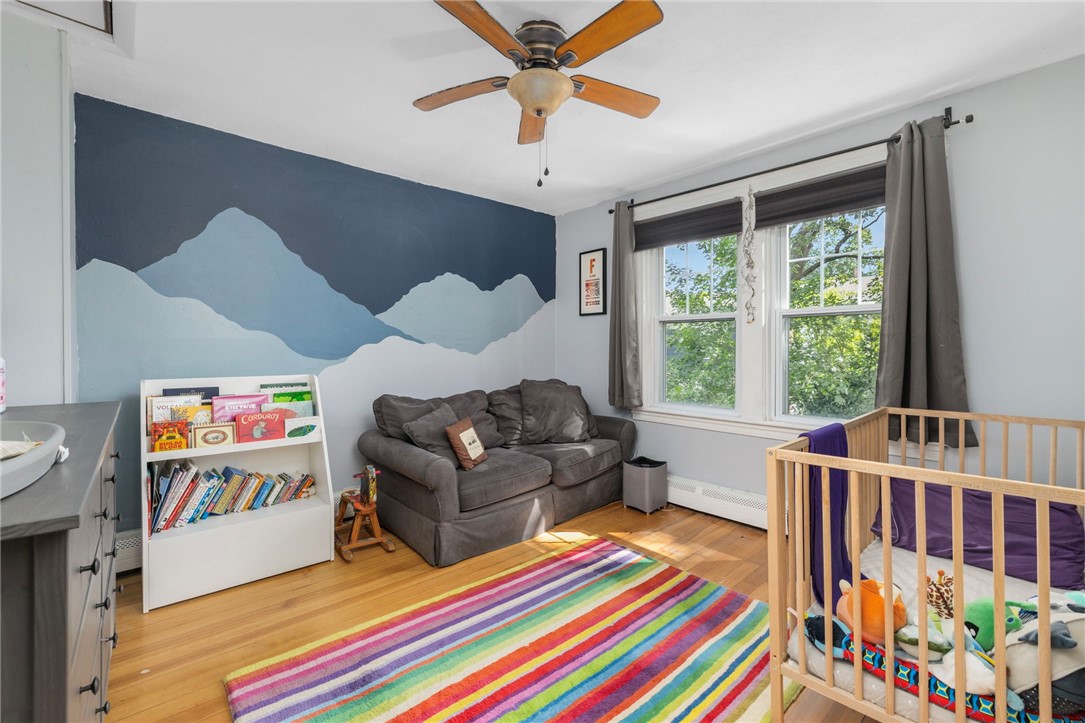 Furnished nursery with a wooden crib, gray sofa, colorful rug, and blue mountain mural.