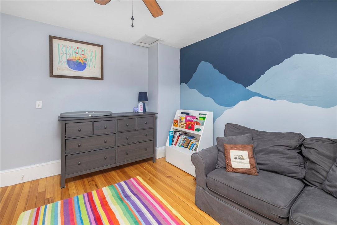 Furnished room with a gray sofa, blue wave mural, children’s book display, and colorful striped rug.