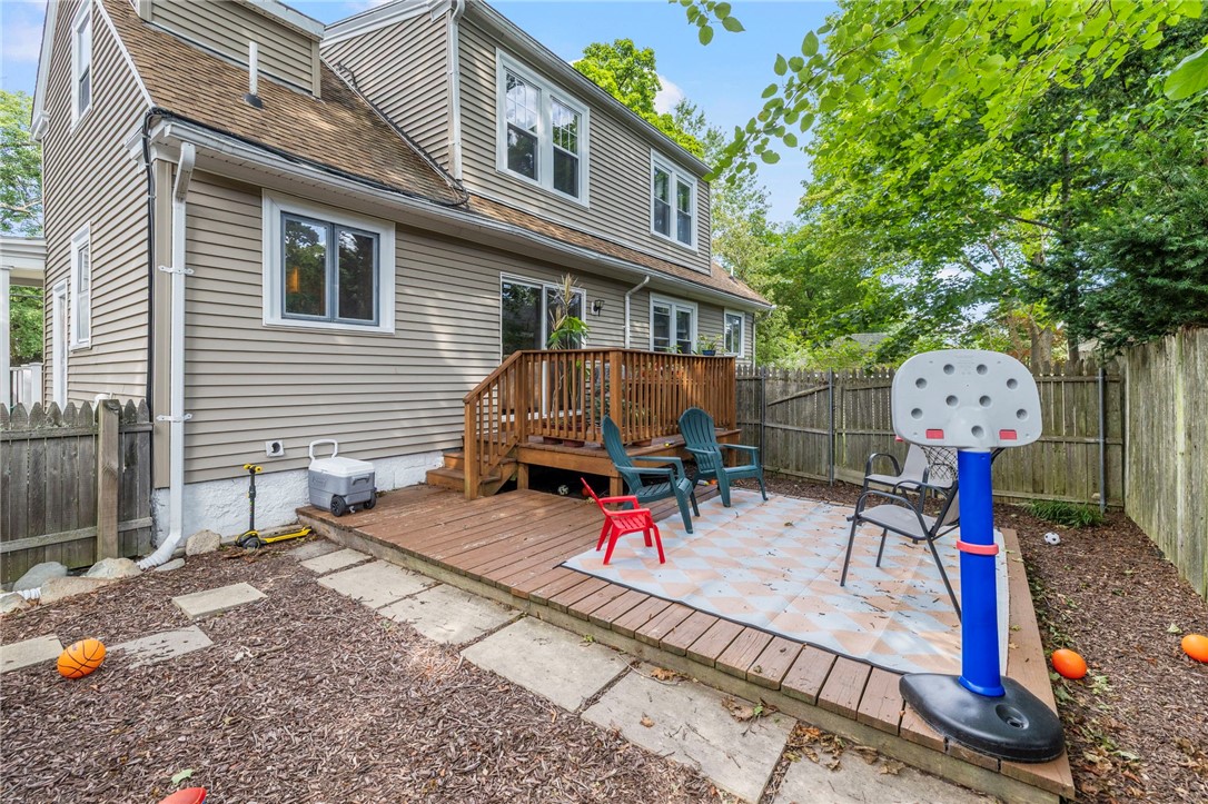 House with a raised wooden deck and fenced backyard patio with chairs and a basketball hoop.