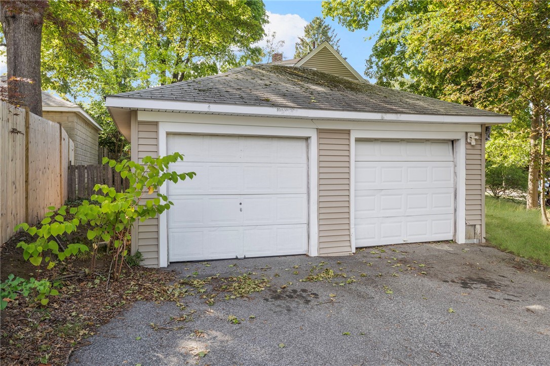 Detached two-car garage with white doors and a paved driveway beneath leafy trees.