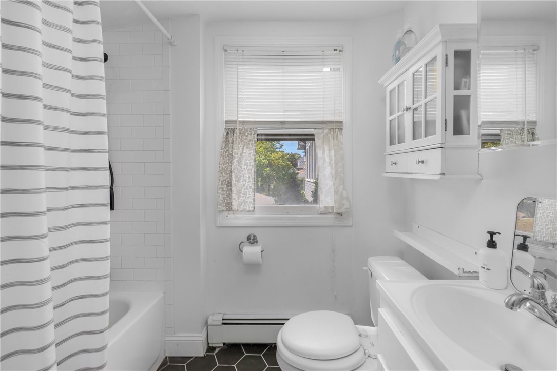 Bathroom with a striped shower curtain, white subway-tile tub, window, and dark hexagonal floor.