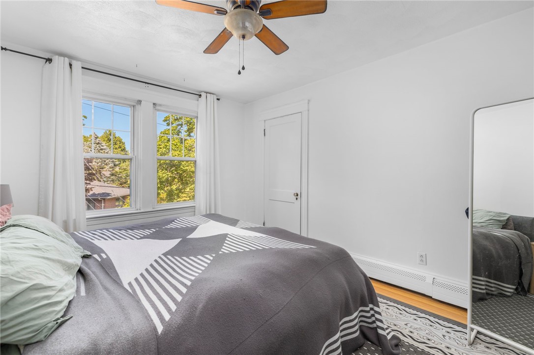 Bedroom with a gray geometric bedspread, two curtained windows, and a ceiling fan.