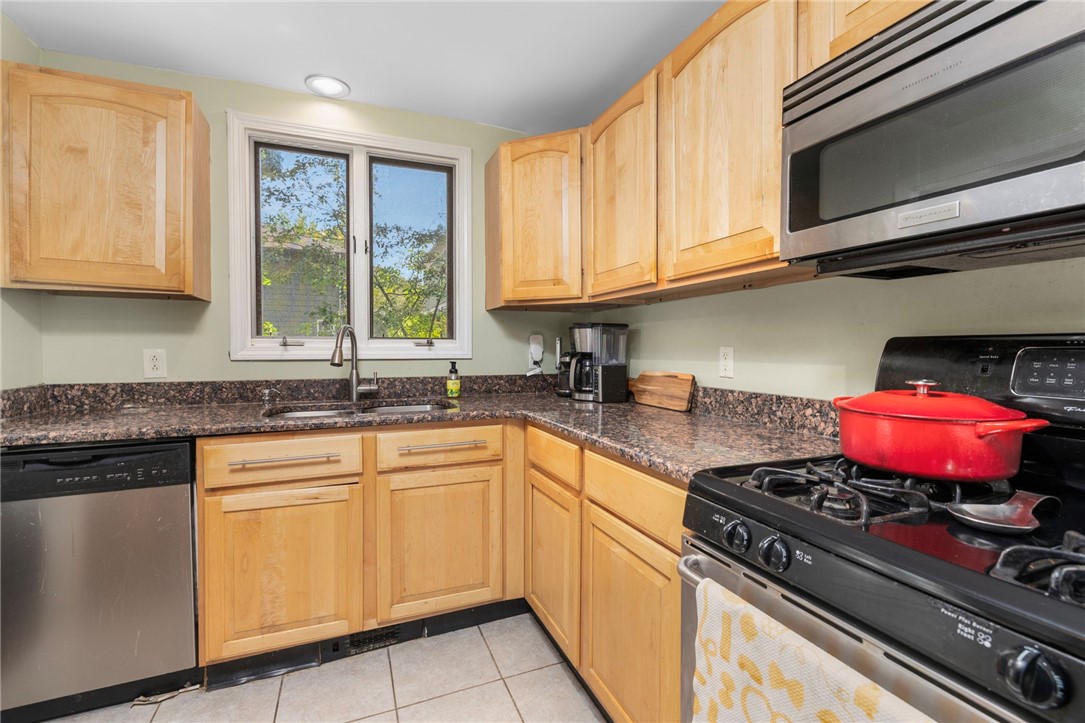 Kitchen with light wood cabinets, granite counters, and a gas range with a red pot.