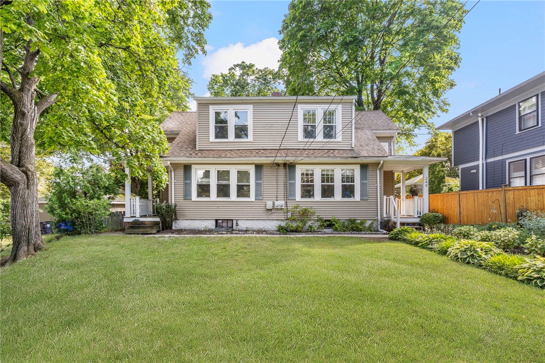 Beige two-story house with a broad front lawn, mature trees, and porches on either side.