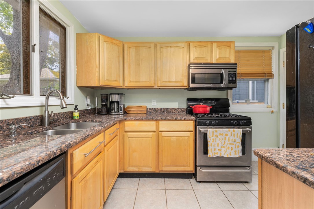 Kitchen with honey-toned wood cabinets, granite counters, stainless appliances, and tiled floor.