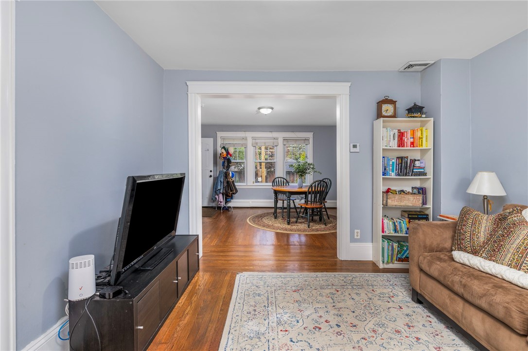 Living room with hardwood floors and patterned rug, opening into a dining area with three windows.