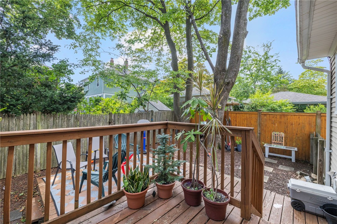 Wooden backyard deck with potted plants and chairs beside a fenced, tree-shaded yard.