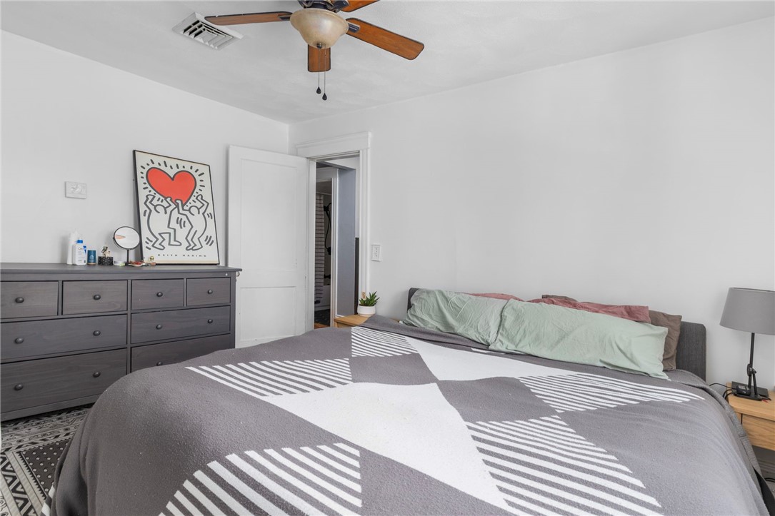 Bedroom with a geometric bedspread, pale green pillows, dark dresser, and framed Keith Haring artwork.