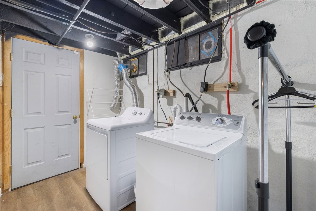 Basement laundry room with a washer and dryer beneath exposed beams and utility pipes.