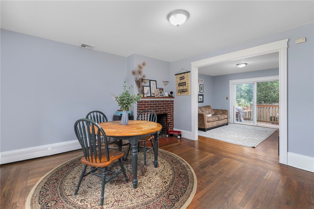 Dining room with a round wooden table, brick fireplace, and doorway to a living room with deck access.