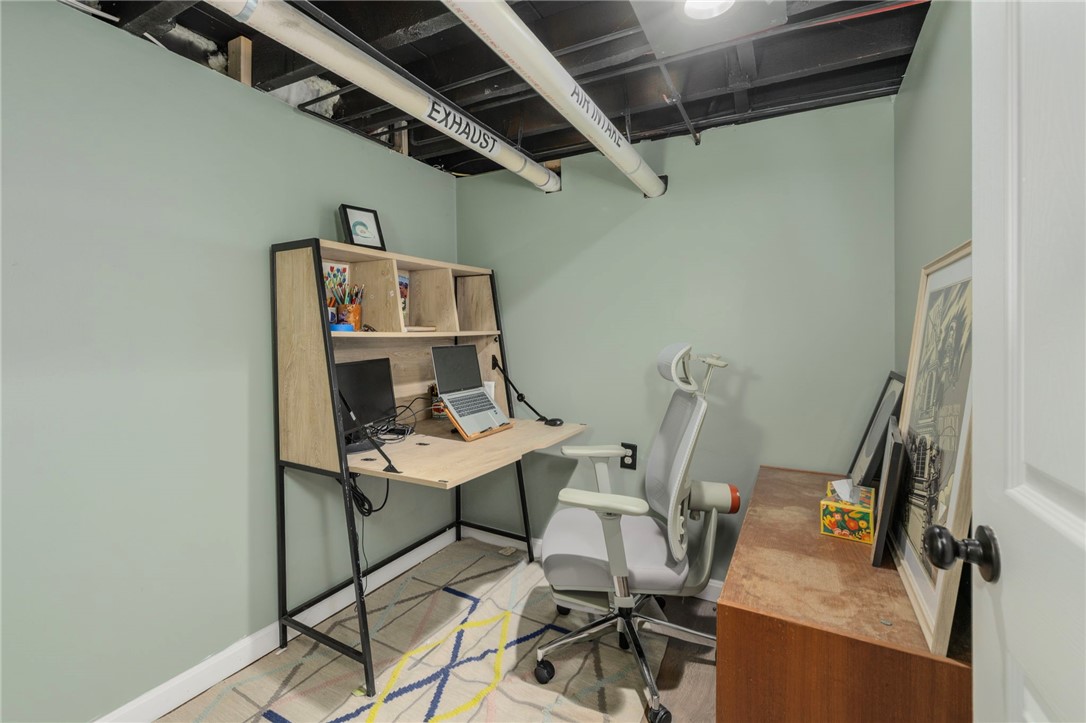 Home office with a desk, computer equipment, ergonomic chair, patterned rug, and exposed ceiling ducts.
