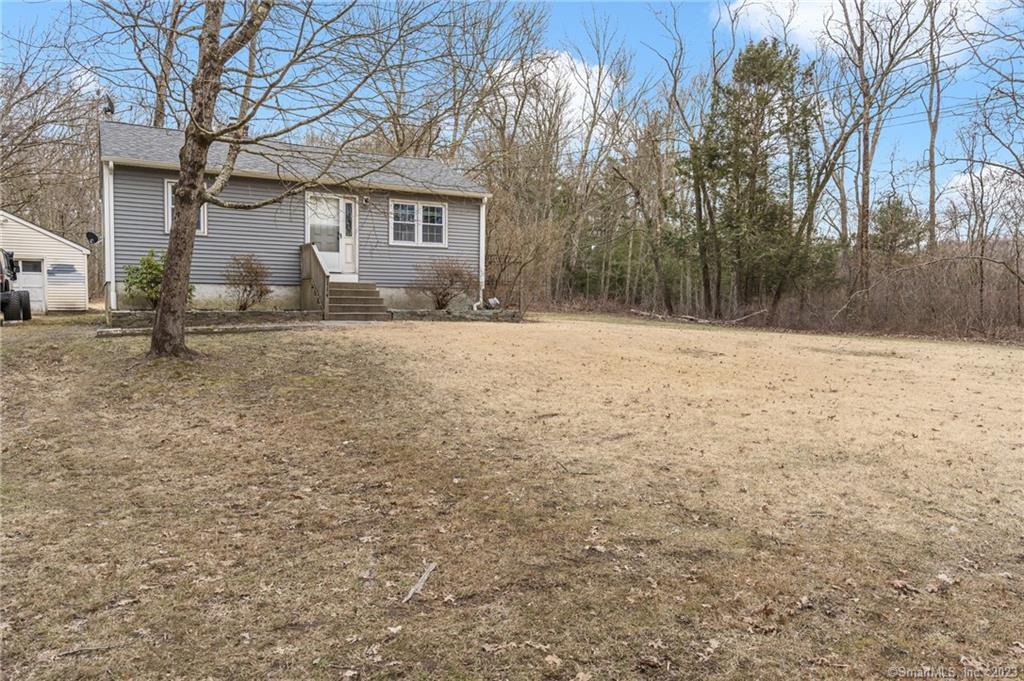 Gray single-story home with front steps, a broad lawn, and leafless trees.
