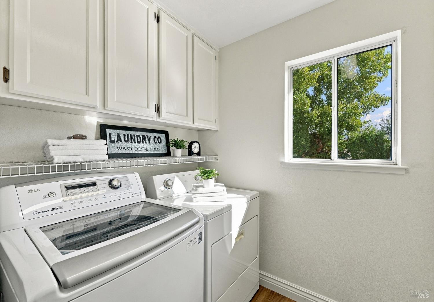 Laundry room with white cabinets, an LG washer and dryer, folded towels, and a sunny window.