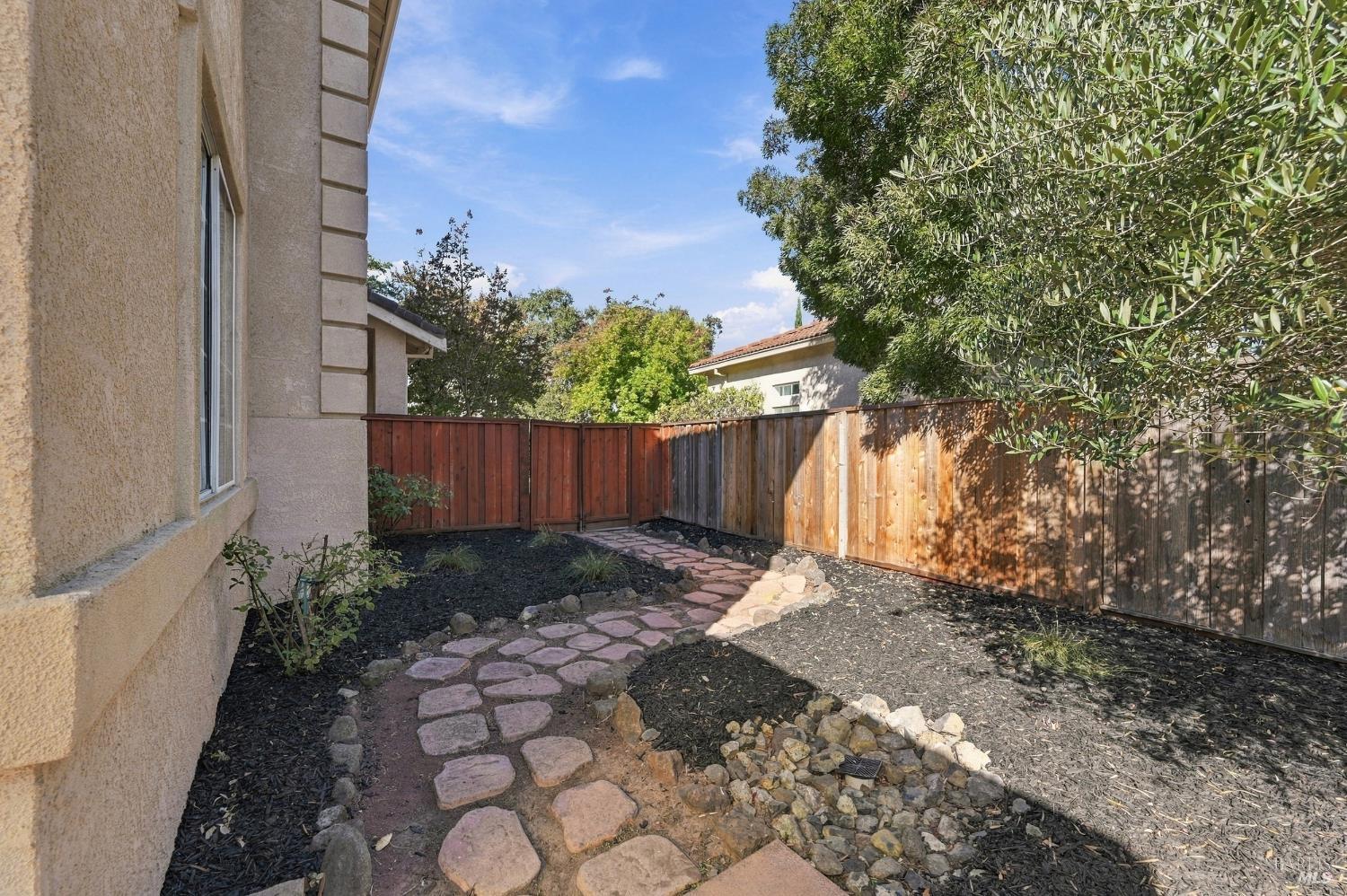 Side yard with a curved stone path, rock landscaping, and a wooden privacy fence.