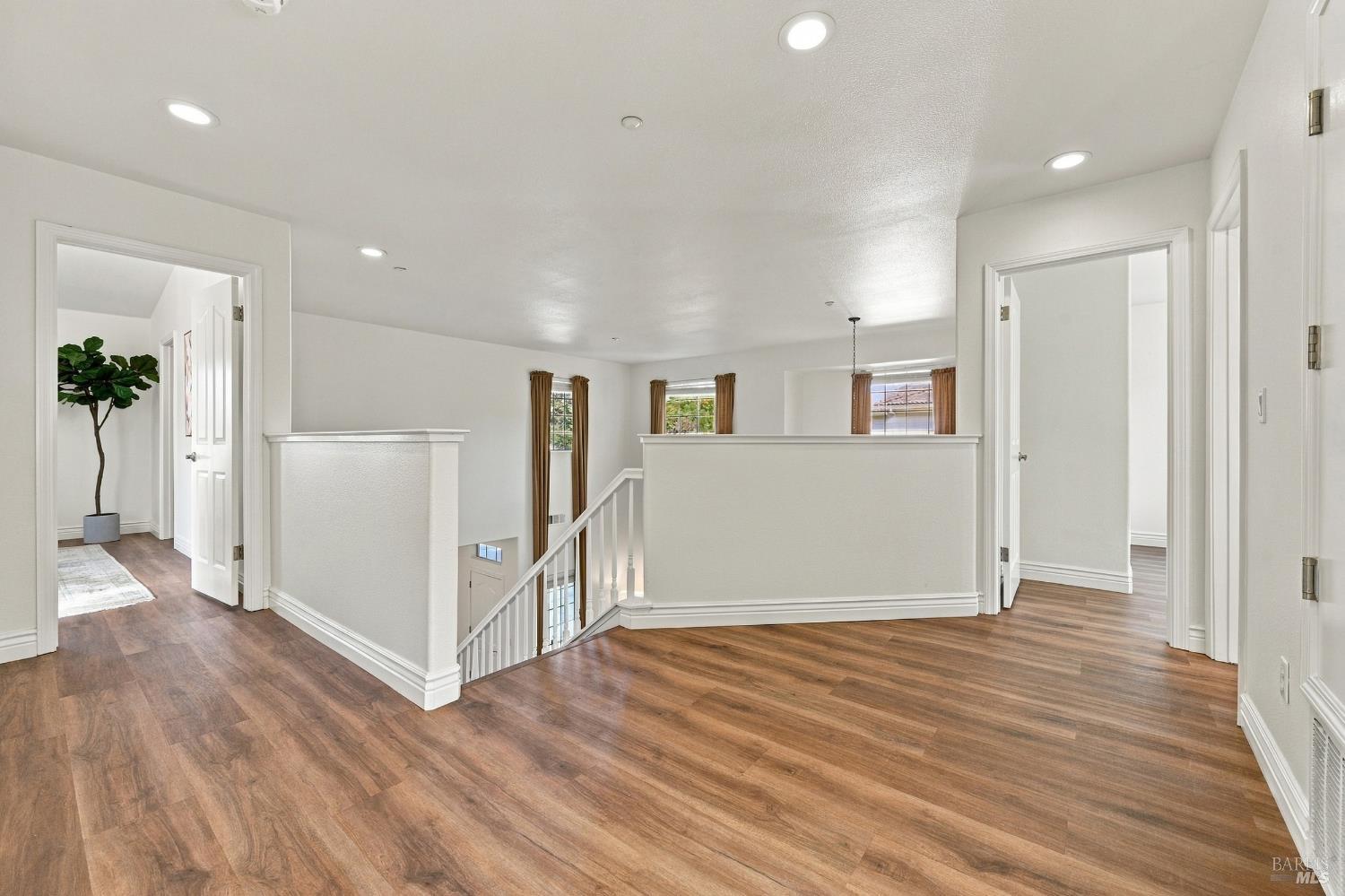 Upstairs landing with wood-look floors, stairwell railing, and windows with brown curtains.