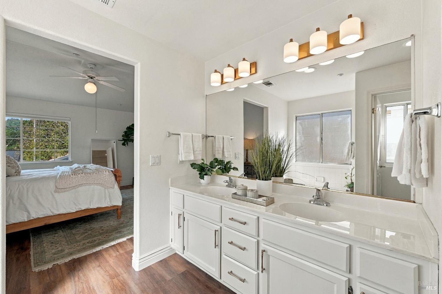 Bathroom with a white double-sink vanity and large mirror, opening to a bedroom.