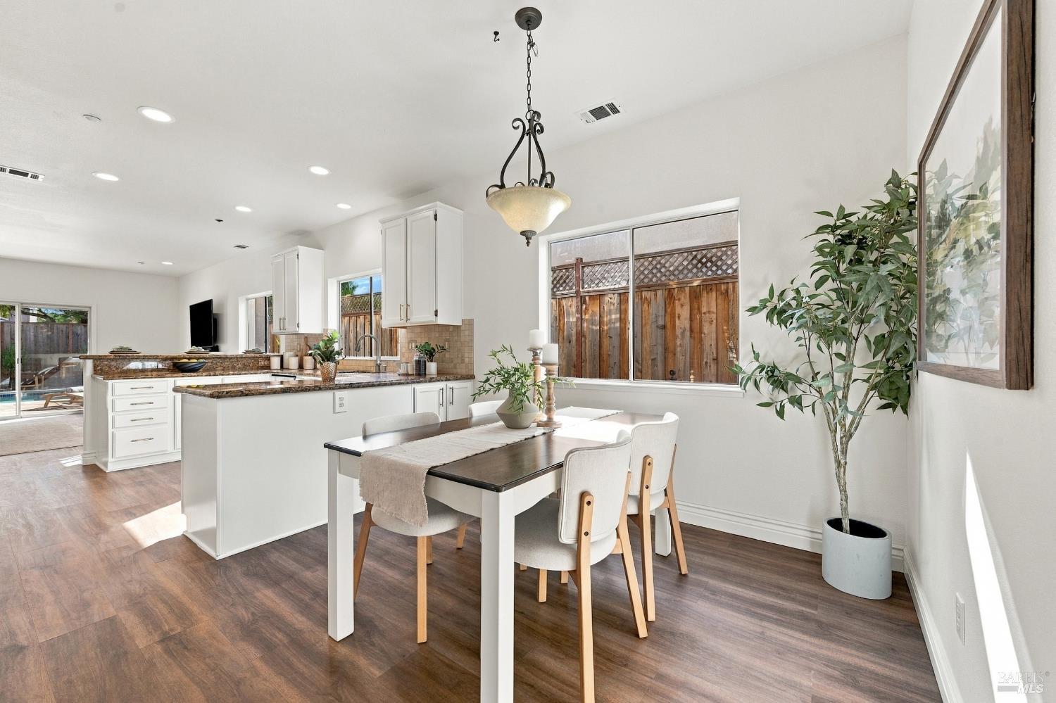Kitchen and dining area with white cabinets, granite counters, and large windows overlooking a fenced yard.