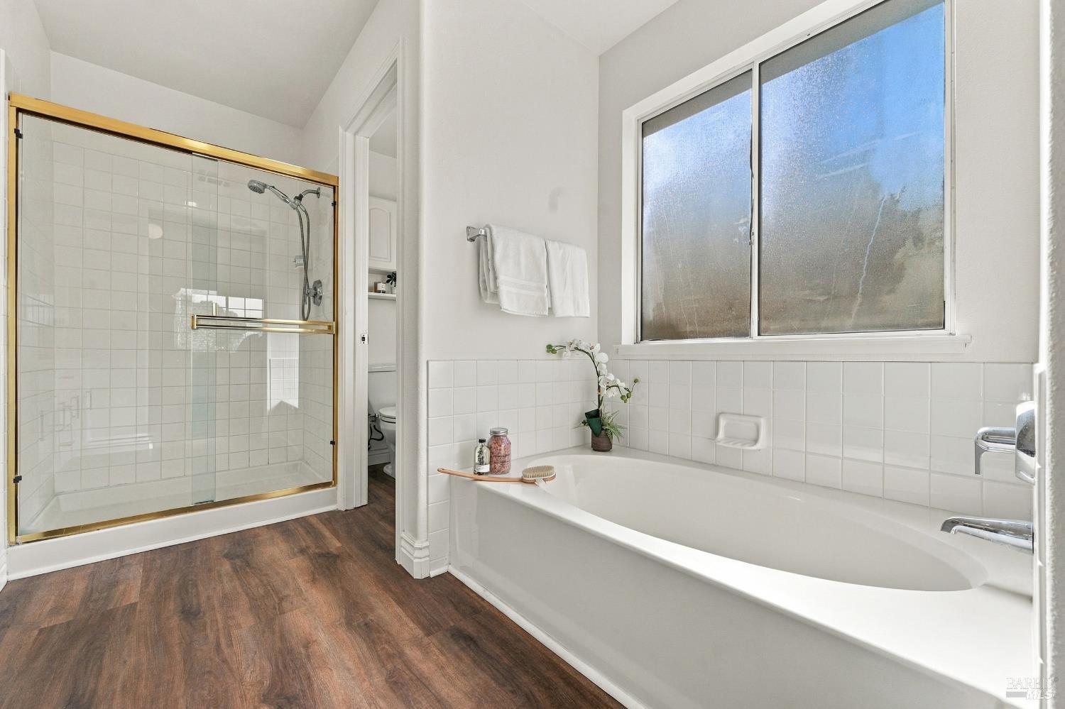 Bright bathroom with a white bathtub, large window, and glass shower with gold-tone trim.