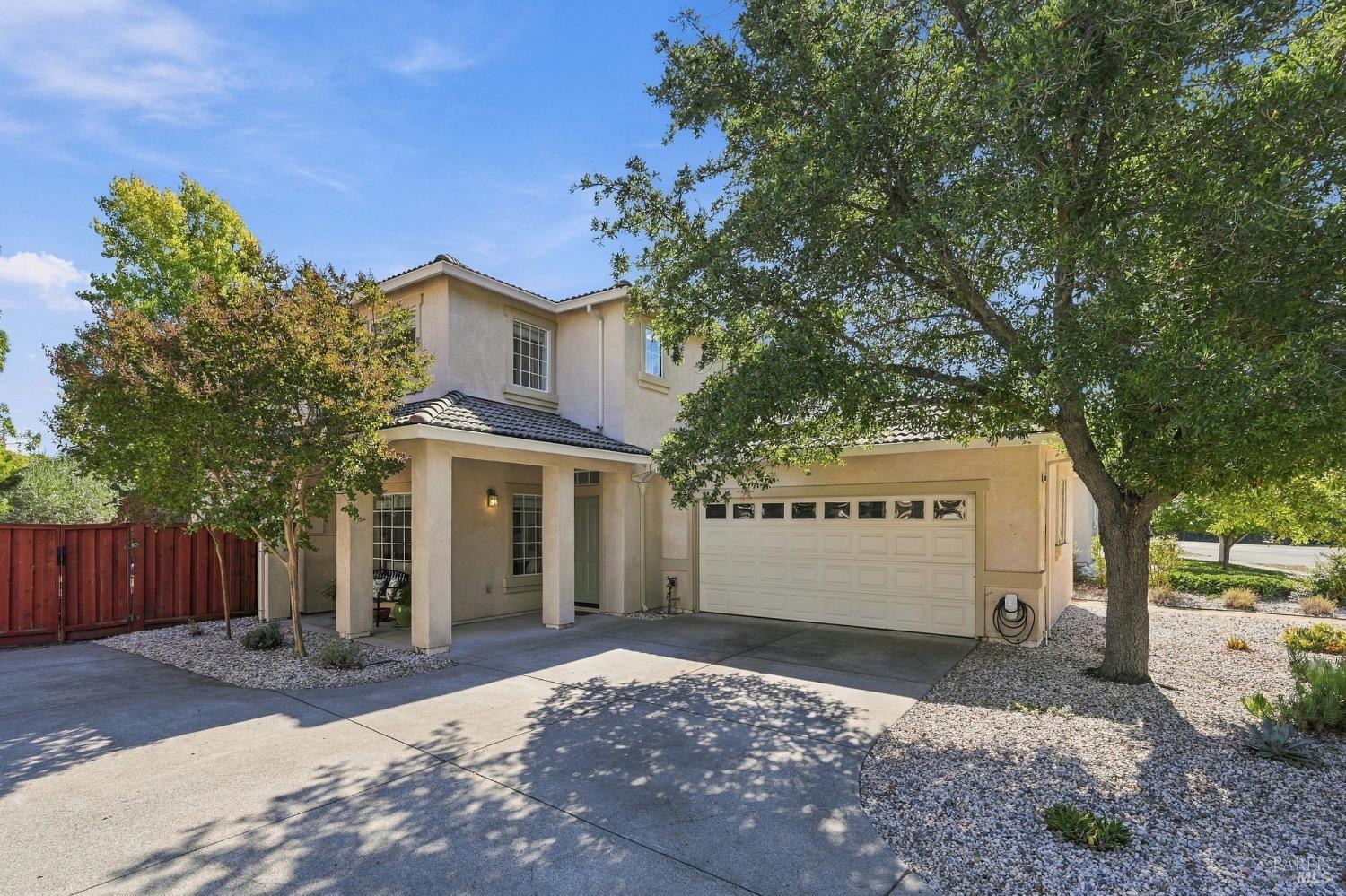 Two-story stucco home with a tiled roof, attached garage, broad driveway, and mature shade trees.