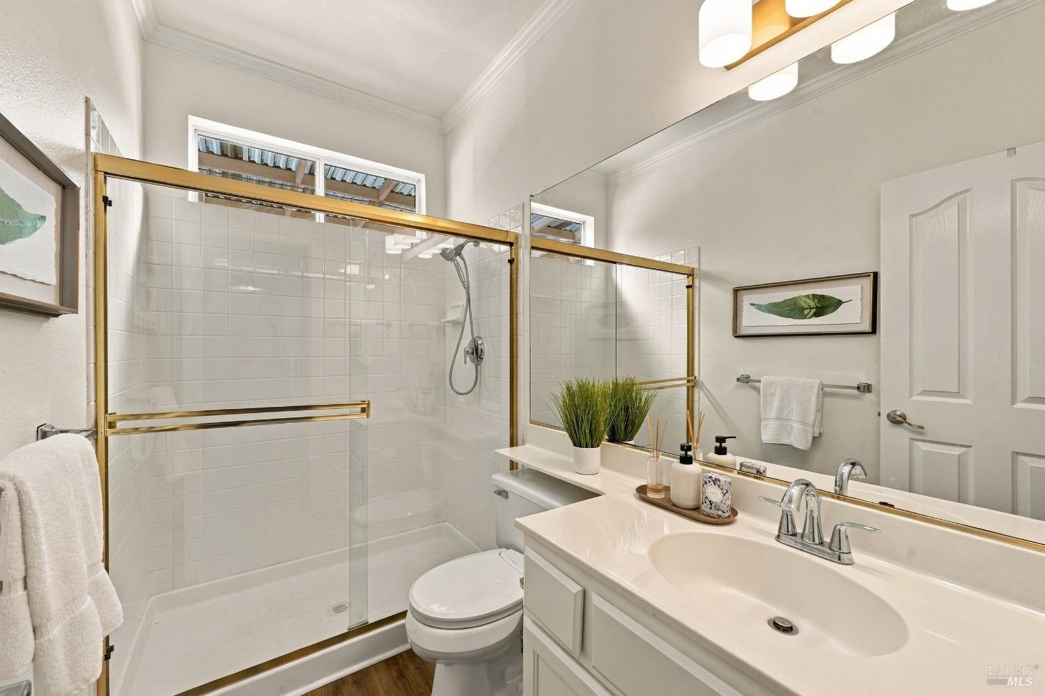 Bathroom with a brass-trimmed glass shower, white tile, and a vanity beneath a large mirror.