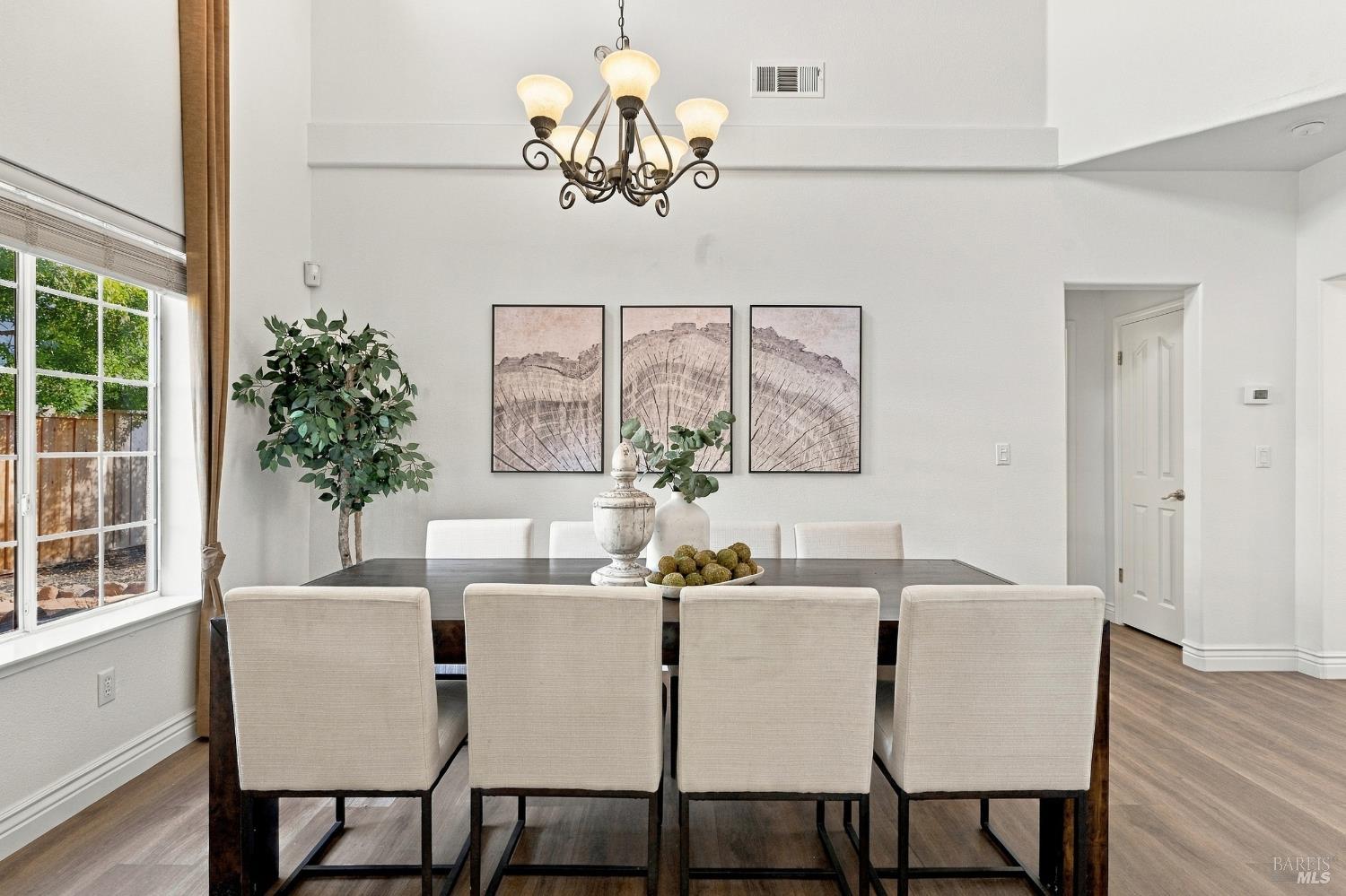Dining room with a dark wood table, cream chairs, wrought-iron chandelier, and large window.