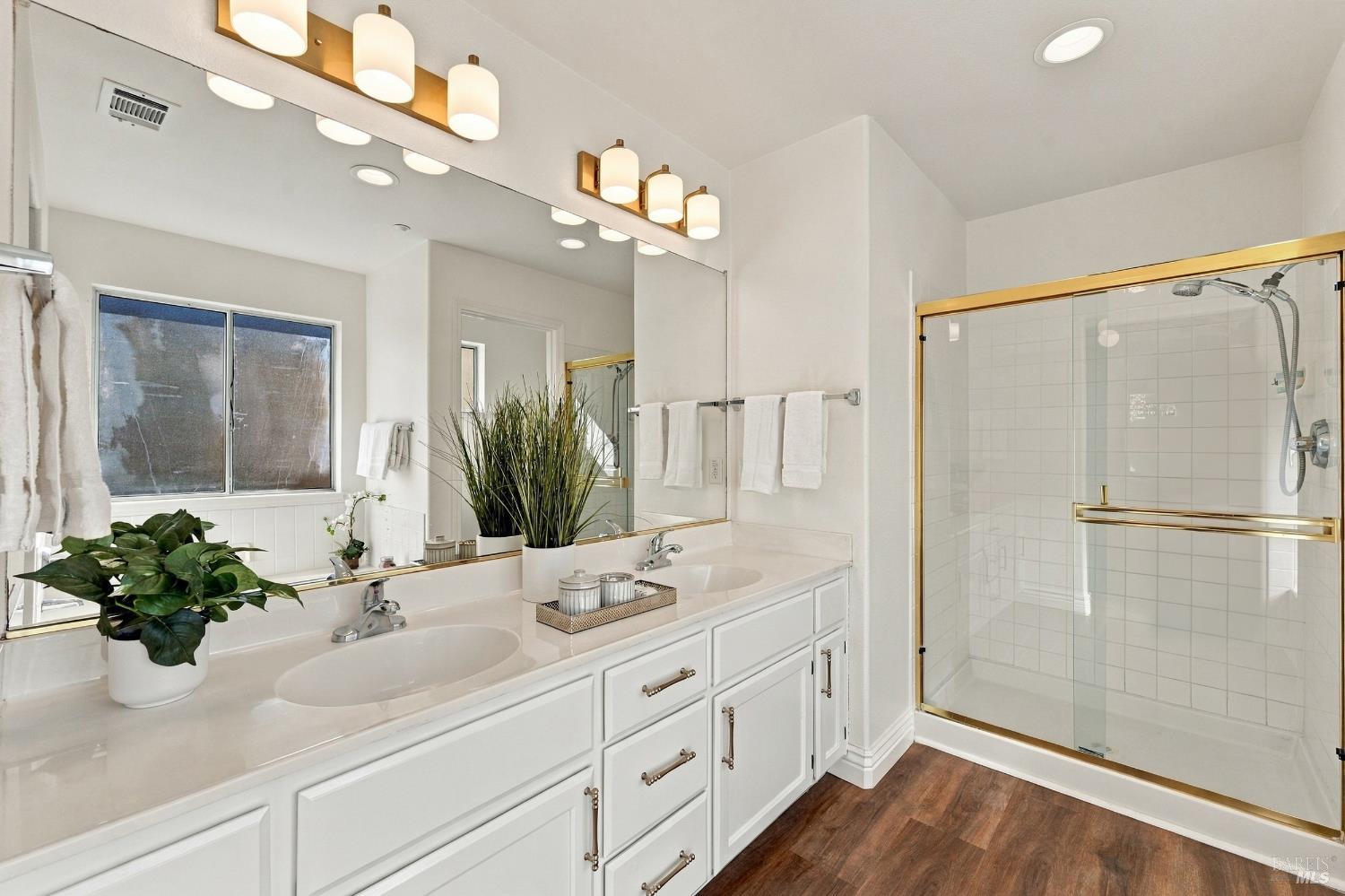 Bright bathroom with a double vanity and a glass shower with gold-toned trim.