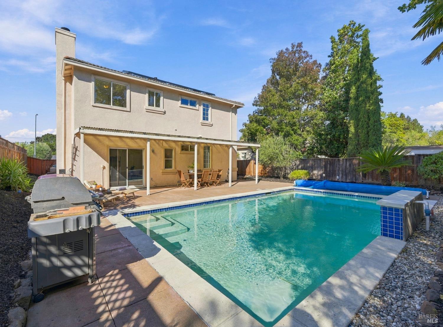Backyard pool beside a two-story stucco home with a covered patio and barbecue grill.
