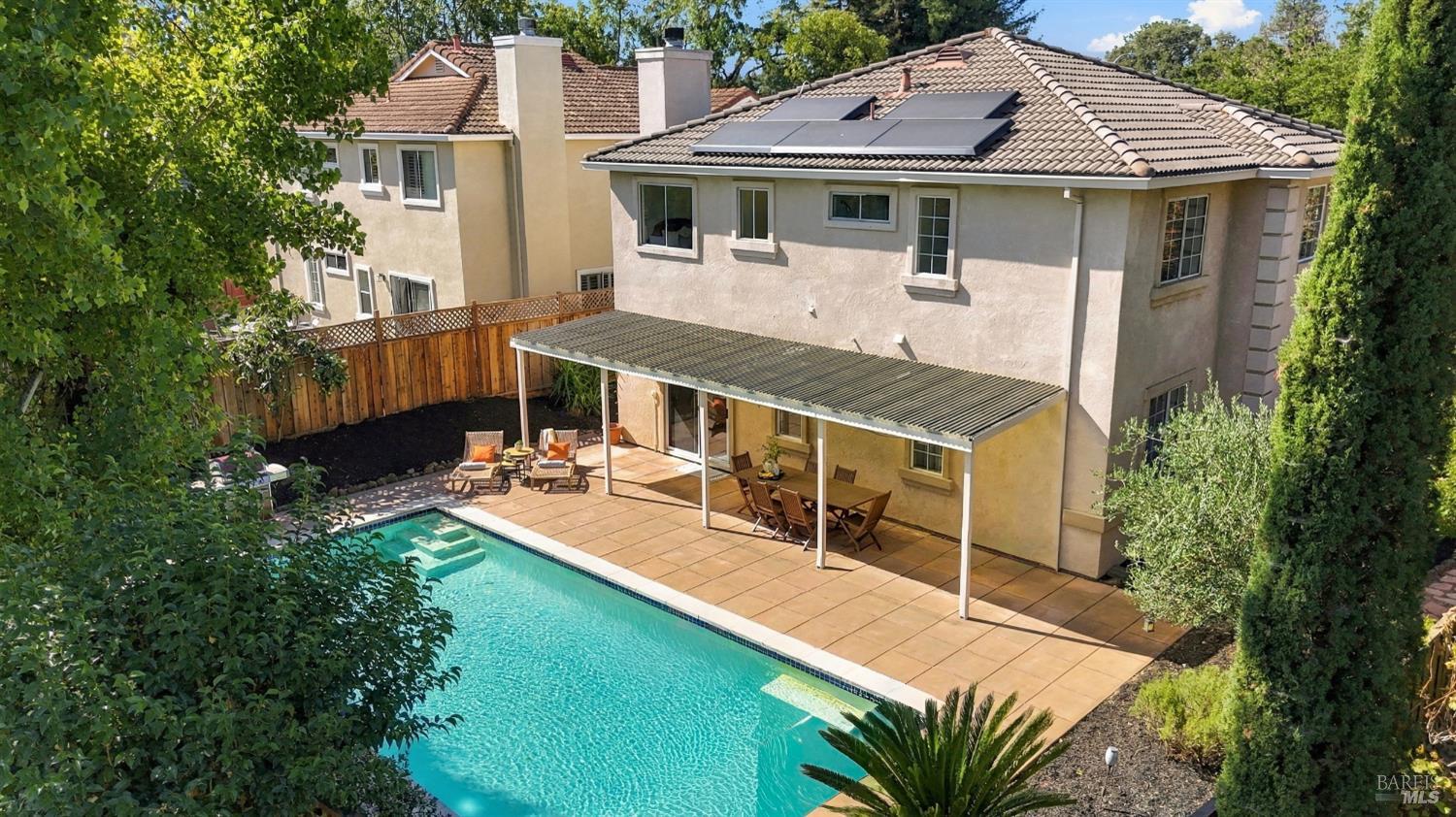 Two-story stucco home with rooftop solar panels overlooking a swimming pool and covered patio.